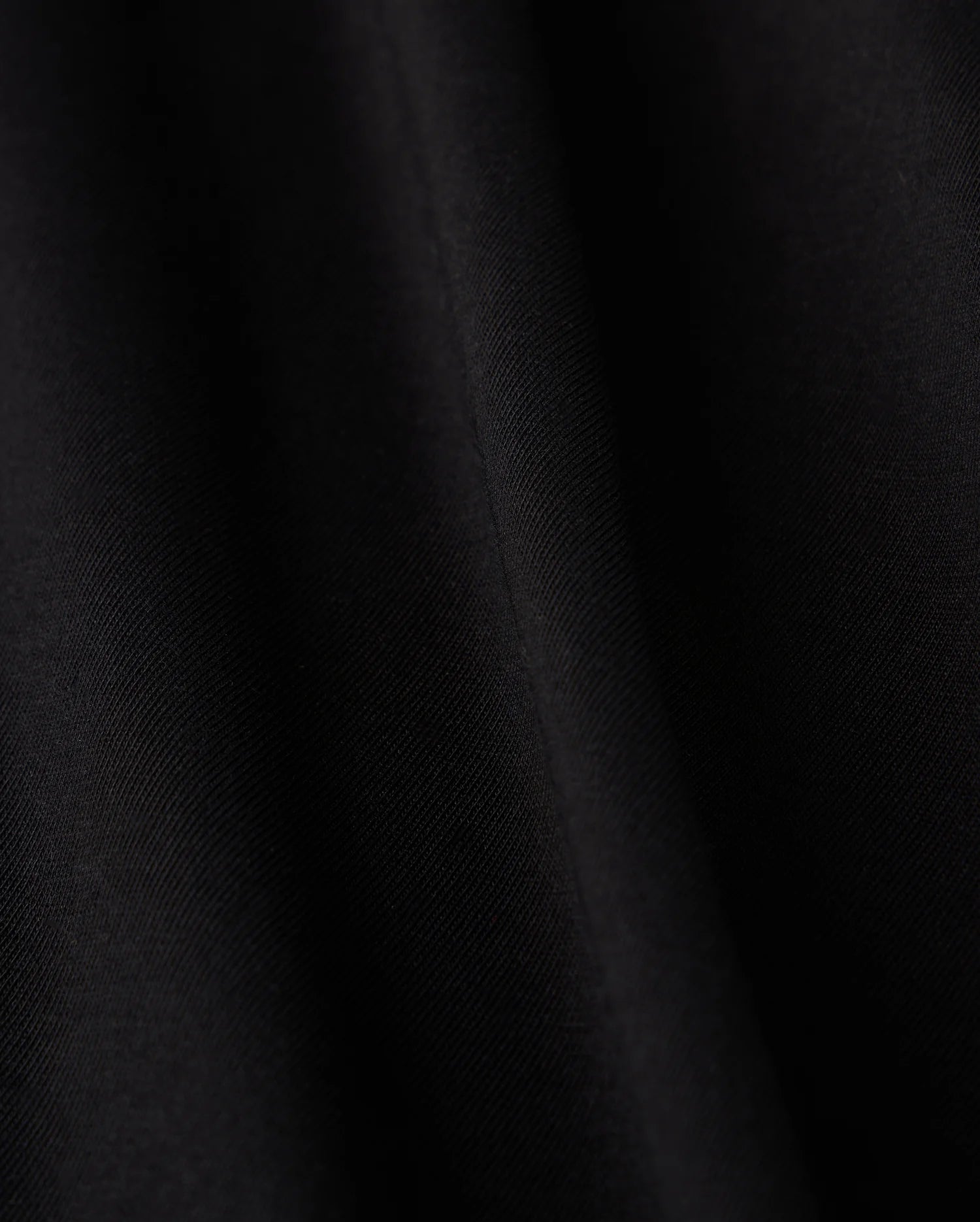 Close-up of a smooth black fabric crafted from luxurious Pima cotton on Psycho Bunny's KIDS HAWAII CITY TEE - B0U169Y1PC, featuring subtle diagonal lines and a soft sheen, evoking the sleek elegance reminiscent of volcanic island landscapes.