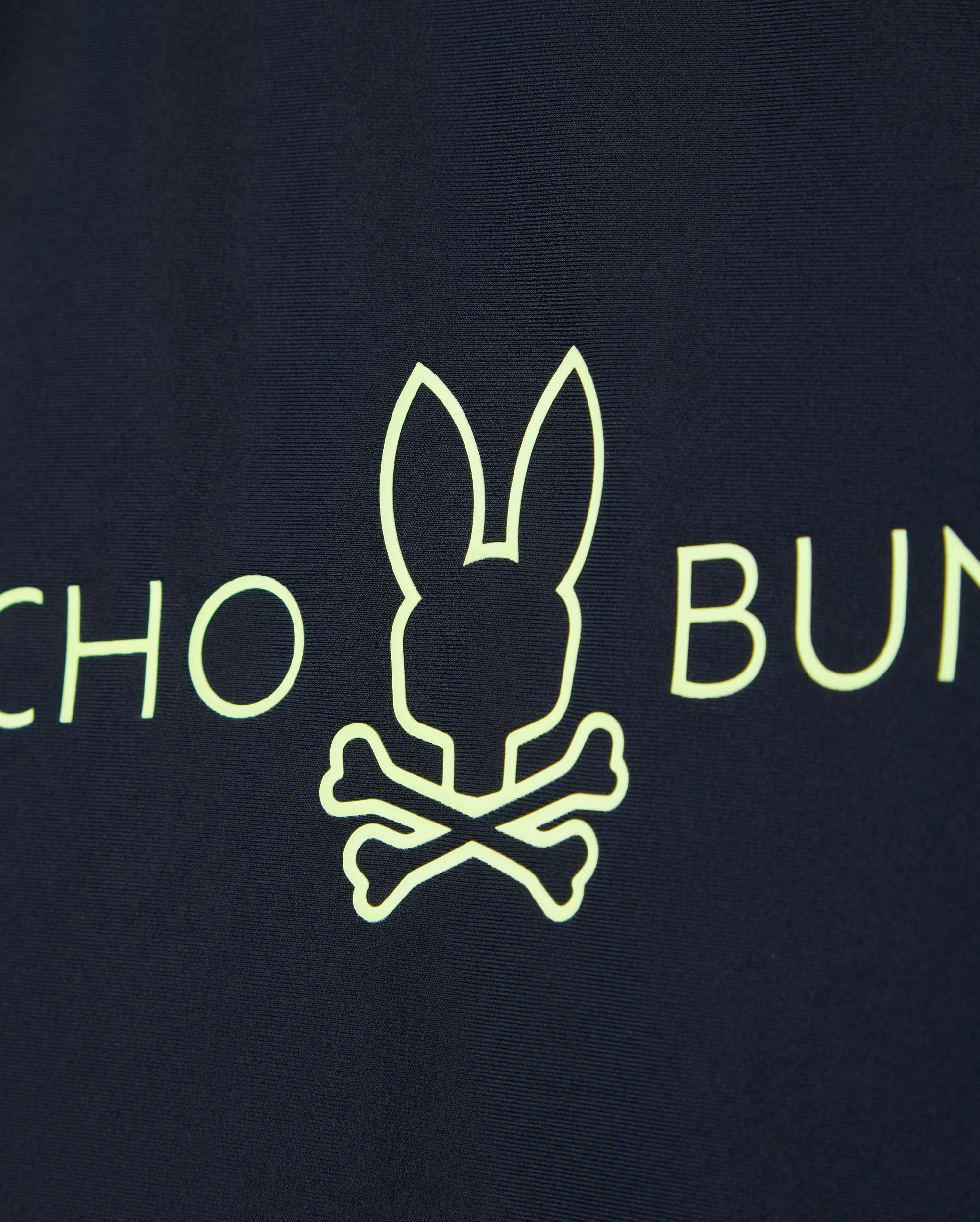 Navy blue fabric of the KIDS SHORT SLEEVE RASH GUARD - B0U558C200 by Psycho Bunny features a neon yellow bunny head above crossed bones with partial text on either side.