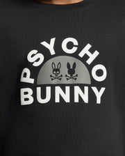 The KIDS GOLDIE GRAPHIC TEE - B0U606F200 from Psycho Bunny is a stylish black tee made of Peruvian Pima cotton, showcasing a bold white "Psycho Bunny" logo and two bunny skulls with crossbones in a semi-circle, perfect for making a statement.