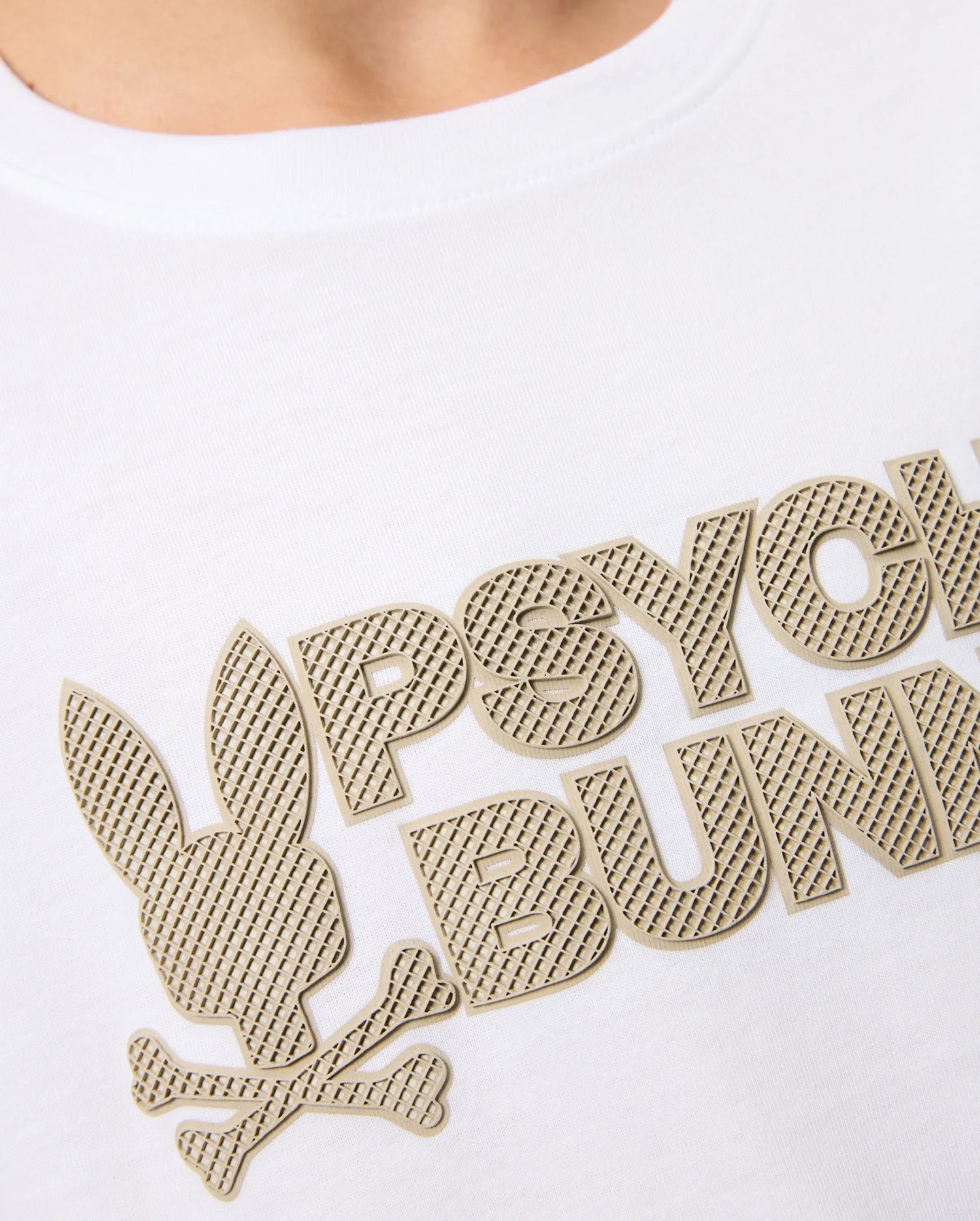 Close-up of a Pima cotton white shirt featuring the Psycho Bunny wordmark and logo. The stylized bunny head with crossbones beneath it is depicted in graphic applications with a textured, patterned design in metallic gold on the KIDS MELVIN GRAPHIC TEE - B0U663C200.