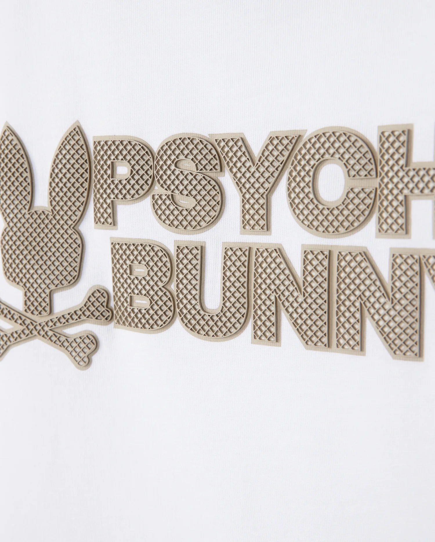 Close-up of the KIDS MELVIN GRAPHIC TEE - B0U663C200 by Psycho Bunny, featuring a white Pima cotton garment with a textured graphic design. The image showcases a stylized bunny head above crossbones, complemented by the words "Psycho Bunny" in large, raised, textured letters. This chic Bunny with wordmark design is primarily rendered in beige.