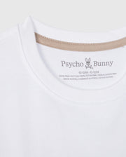 A close-up photo of a white Psycho Bunny KIDS MELVIN GRAPHIC TEE - B0U663C200. The image focuses on the collar area, showing brand details and size information, with a Bunny with wordmark printed on the inner neck label. The shirt is made of 100% Pima cotton and it is made in Peru.