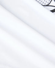 Close-up of smooth, white fabric with a subtle fold and a part of a black geometric pattern visible at the top right corner. The texture appears soft and slightly reflective under the lighting, reminiscent of a high-quality performance-led jersey, much like the Psycho Bunny KIDS COURTSIDE GRAPHIC TEE - B0U681C200.