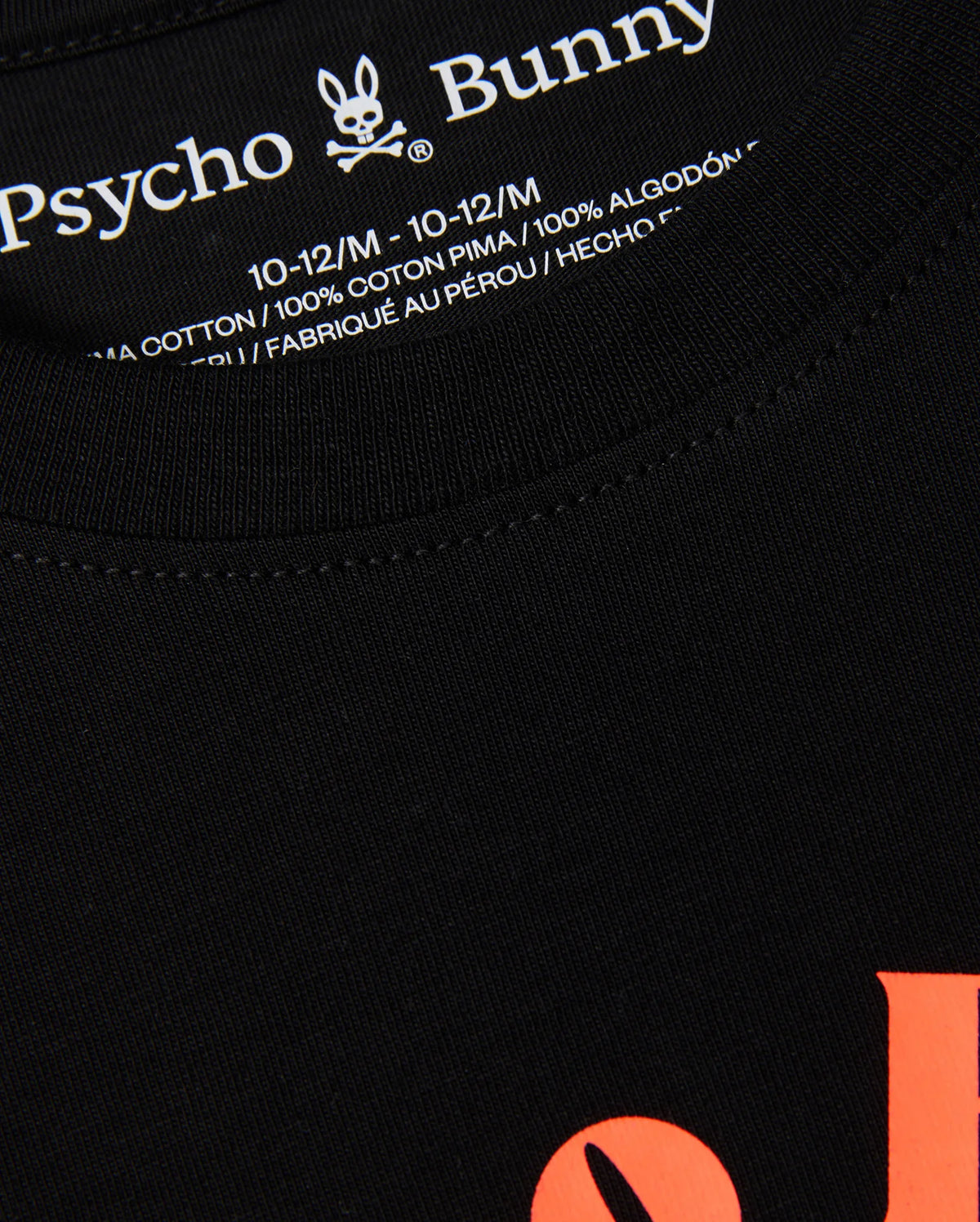 Close-up of the label on a black KIDS COURTSIDE GRAPHIC TEE - B0U682C200 by Psycho Bunny, showing size 10-12/M in white text. This kids' graphic tee boasts orange lettering on the front and is crafted from 100% pima cotton. Made in Peru, this tennis-inspired piece combines style and comfort.