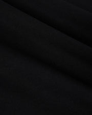 Close-up of the smooth, folded fabric of the KIDS COURTSIDE GRAPHIC TEE by Psycho Bunny in black, showcasing a subtle texture akin to a performance-led jersey. The material looks soft and slightly glossy, with gentle curves creating lines across the surface.