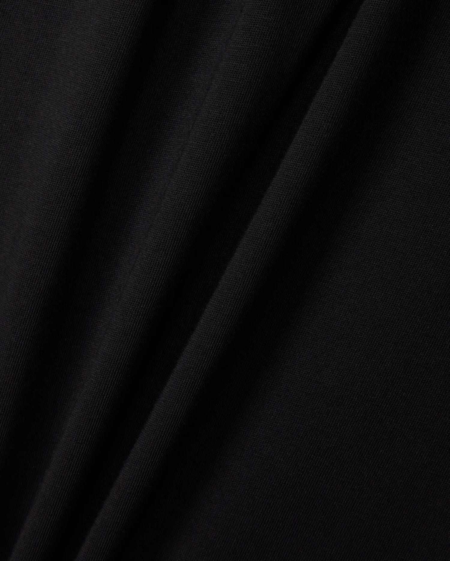 Close-up of a black Pima cotton fabric exhibiting gentle folds and a smooth texture, highlighting the delicate interplay of light and shadow across the material, reminiscent of a finely crafted KIDS ZACK GRAPHIC TEE by Psycho Bunny.