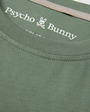 Close-up of a KIDS ZACK GRAPHIC TEE in green, made from luxurious Pima cotton by Psycho Bunny, featuring the iconic bunny and crossbones logo printed on the inner neckline.