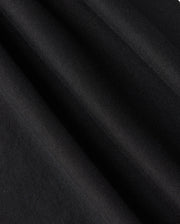 Experience a close-up view of the black Pima cotton fabric featured in the KIDS TACOMA GRAPHIC TEE - B0U909D200 by Psycho Bunny, showcasing a subtle diagonal texture that creates a smooth, elegant surface. The folds of the tee suggest movement and depth, hinting at exquisite embroidered details.