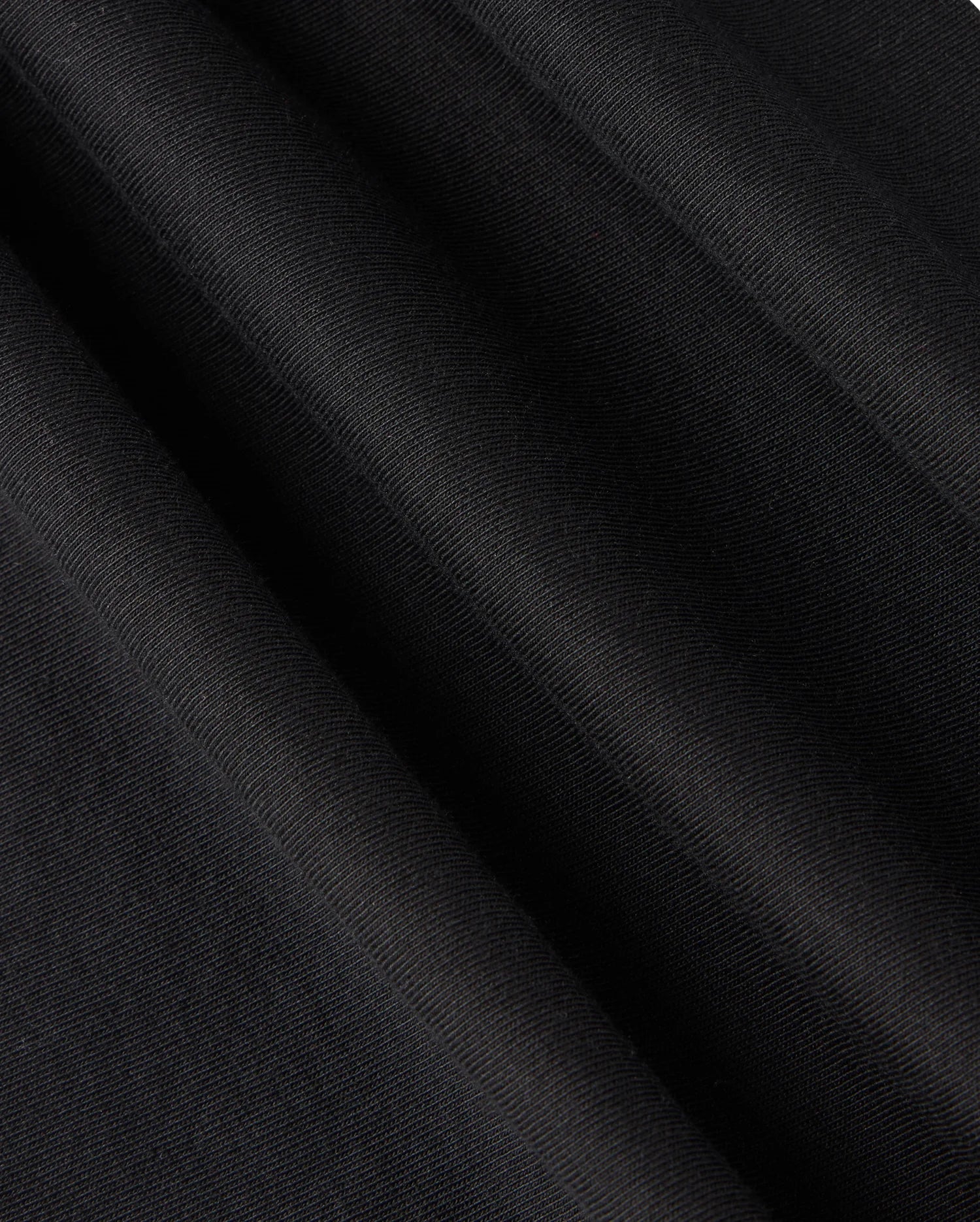 Experience a close-up view of the black Pima cotton fabric featured in the KIDS TACOMA GRAPHIC TEE - B0U909D200 by Psycho Bunny, showcasing a subtle diagonal texture that creates a smooth, elegant surface. The folds of the tee suggest movement and depth, hinting at exquisite embroidered details.