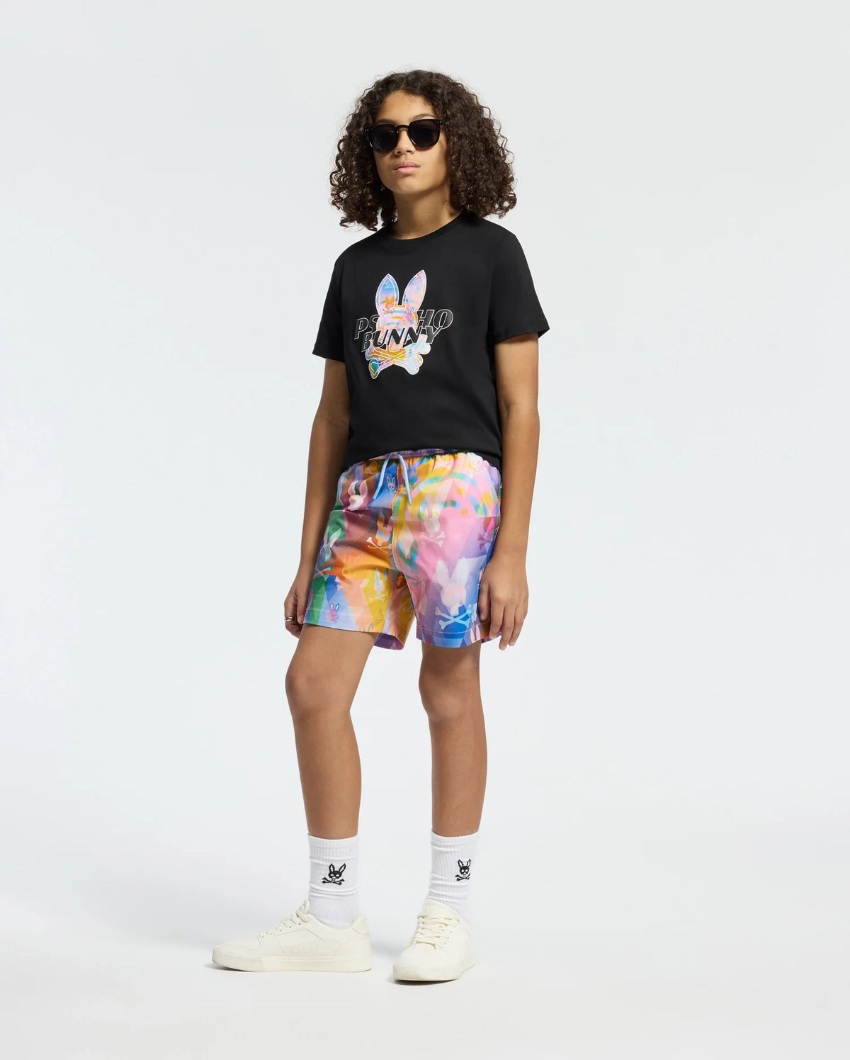 Black psycho bunny graphic tee with a colorful bunny skull design on the chest, paired with vibrant tie-dye swim shorts featuring an all-over bunny skull pattern and white socks with a small logo.