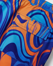 Close-up of the KIDS NEVADA ALL OVER PRINT SWIM TRUNK - B0W526C200 by Psycho Bunny, showcasing its vibrant, swirling blue and orange pattern. The quick-dry fabric features an elastic waistband and a pocket with a flap, indicative of swim trunks. The design exhibits a retro, psychedelic feel.