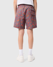 A person wearing gray KIDS SHELDON ALL OVER PRINT SWIM TRUNK - B0W588C200 by Psycho Bunny with a red bunny pattern is seen from behind. The shorts, made of quick-dry fabric, feature an elastic waistband and a back pocket. The individual also wears white socks, white sneakers, and a white t-shirt. The background is plain and light gray.