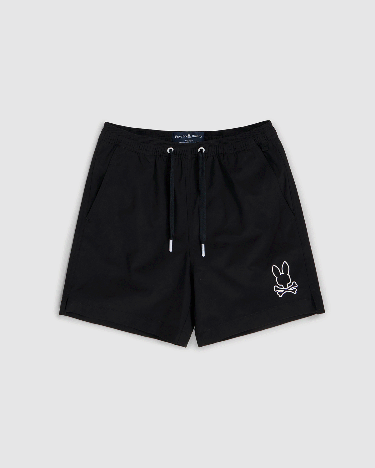 Black shorts featuring a white outline of a bunny with crossbones on the bottom right corner. Made from quick-dry material, these shorts have an elastic waistband with a black drawstring and two side pockets. Ideal for summer, the **KIDS PARKER HYDROCHROMIC SWIM TRUNK - B0W646C200** design by **Psycho Bunny** blends style and function against a light gray background.