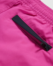 Close-up of the KIDS PARKER HYDROCHROMIC SWIM TRUNK - B0W646C200 by Psycho Bunny, showcasing its bright pink fabric with a pocket design. The pocket features a black zipper that is partially opened, revealing an inner layer. The smooth and shiny texture of the fabric is reminiscent of high-quality swim trunks. The stitching around the pocket is also clearly visible.