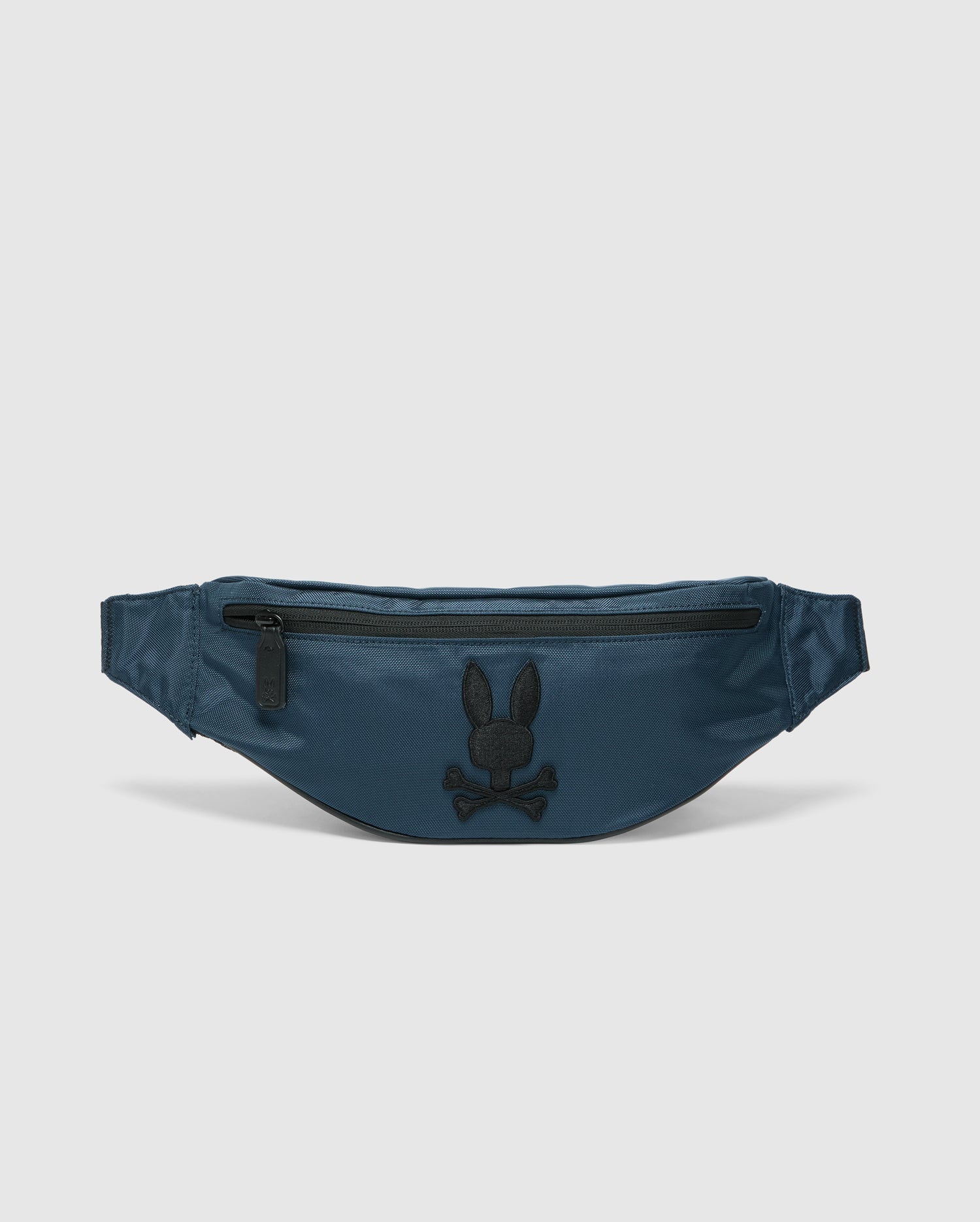 The Psycho Bunny MENS CROSS BODY BAG - B6A181E200, crafted from blue nylon, features a black zipper and an embroidered rabbit head logo above crossed bones in black on the front, making it the perfect functional waist bag for men.