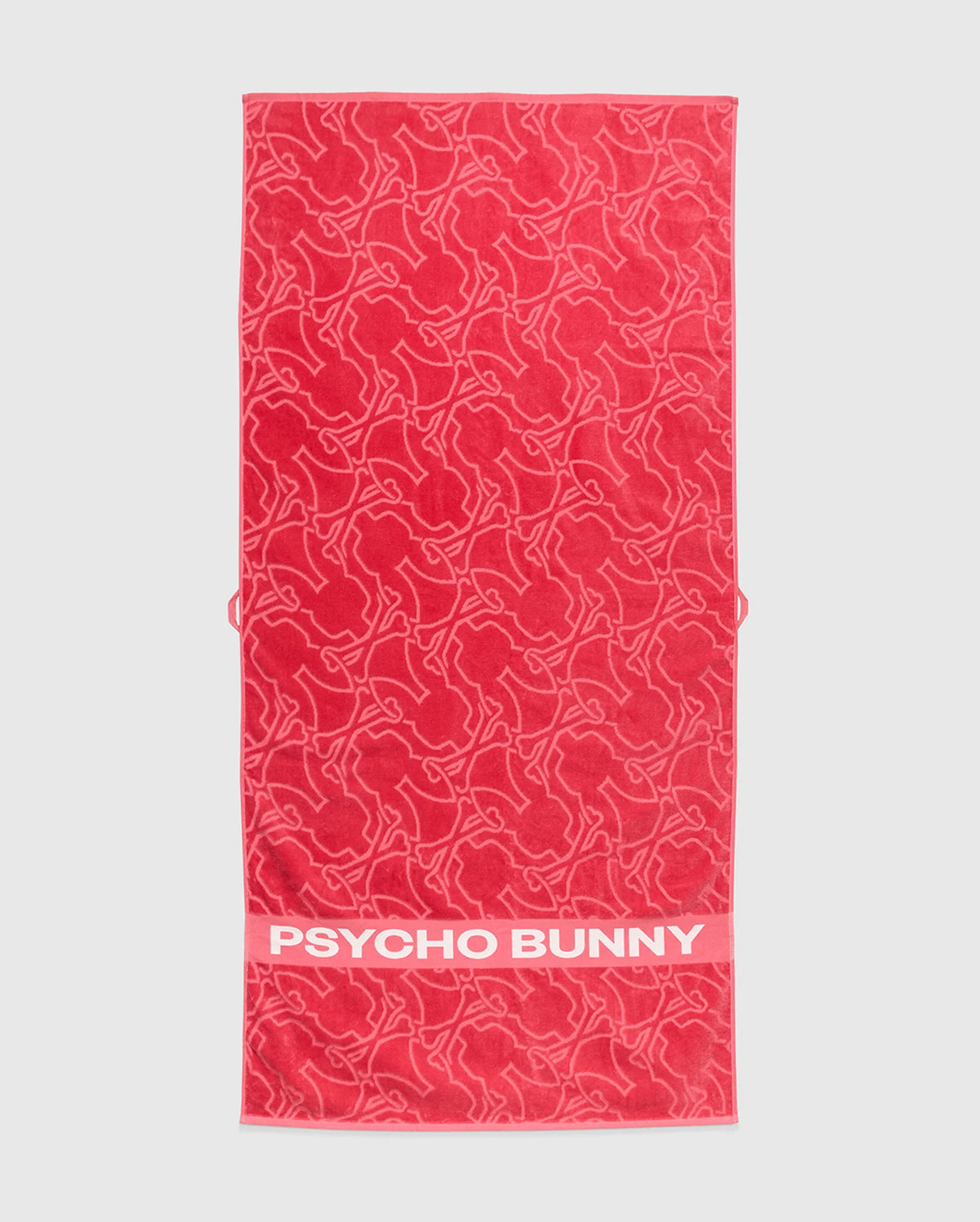 A red Psycho Bunny towel, model B6A287F200, is crafted from plush terrycloth cotton. It features abstract bunny designs and a solid red band at the bottom edge with the iconic white "PSYCHO BUNNY" text, merging style and comfort in premium apparel.