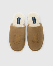 These men's suede slippers from Psycho Bunny feature a brown cow suede leather exterior and a plush white fleece lining. The embroidered rabbit skull and crossbones add a distinctive flair to the genuine shearling comfort they provide.