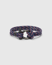 The Psycho Bunny MEN'S ROPE BRACELET - B6A368E200 features a chic braided nylon design in navy and red with metal accents and engraved text. Its circular coil on a plain background makes it a modern, must-have accessory for any man's wardrobe.