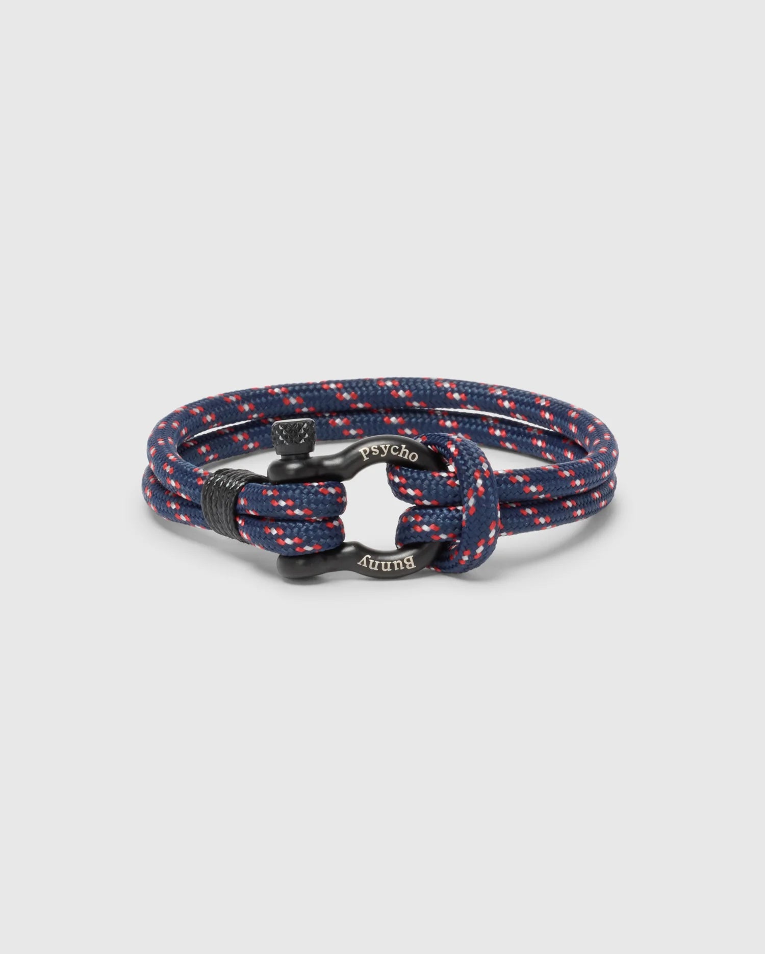 The Psycho Bunny MEN'S ROPE BRACELET - B6A368E200 features a chic braided nylon design in navy and red with metal accents and engraved text. Its circular coil on a plain background makes it a modern, must-have accessory for any man's wardrobe.