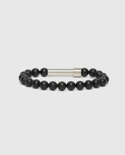 A high-quality men's bead bracelet, model B6A370E200 by Psycho Bunny, is showcased on a plain white background. This fashionable accessory includes uniformly sized round black beads and features a sleek cylindrical silver clasp for fastening.
