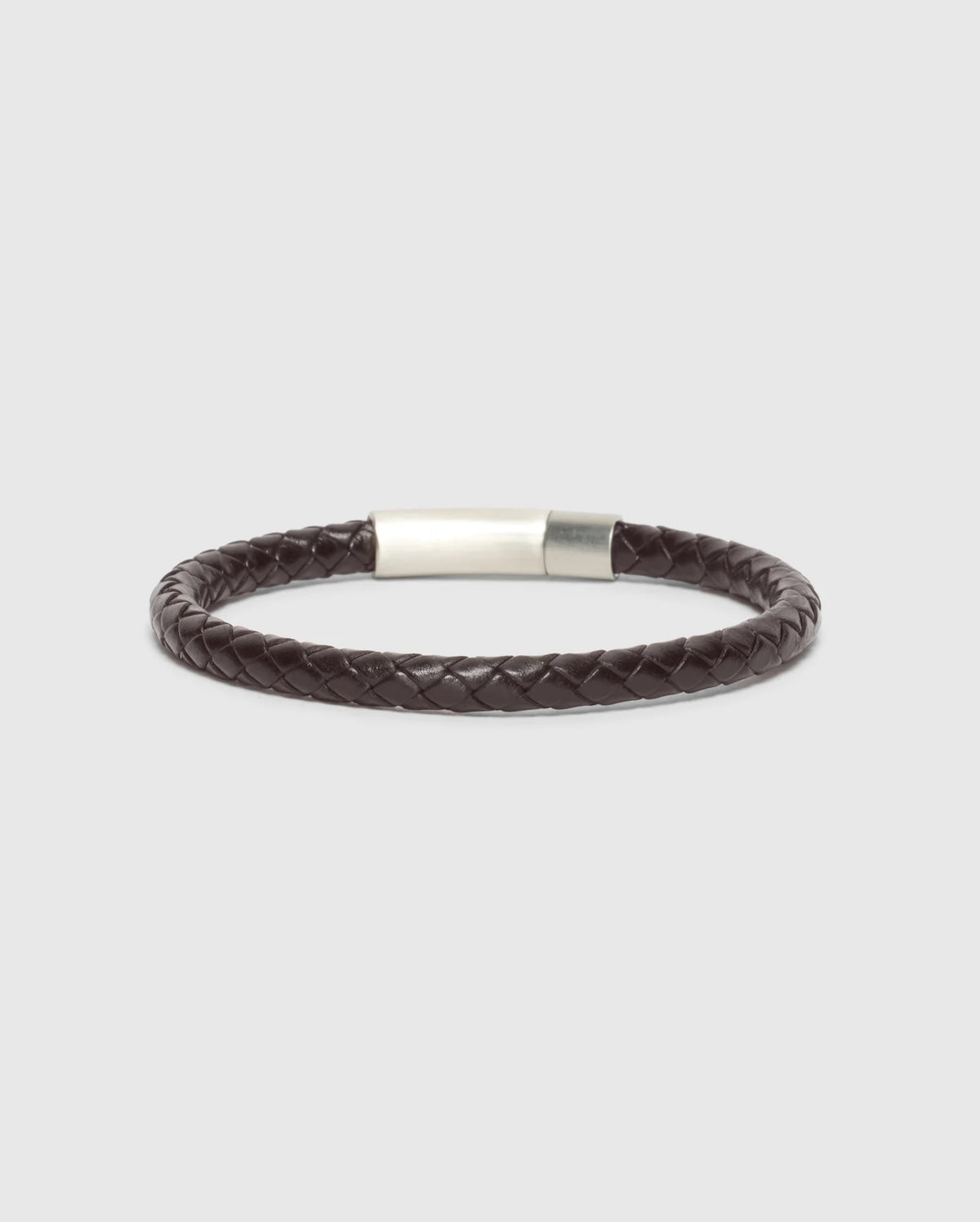 A stylish and elegant accessory, the MEN'S BRAIDED LEATHER BRACELET - B6A371E200 from Psycho Bunny showcases a sophisticated dark brown braided leather design with a sleek polished silver clasp, set against a minimalist light gray backdrop.
