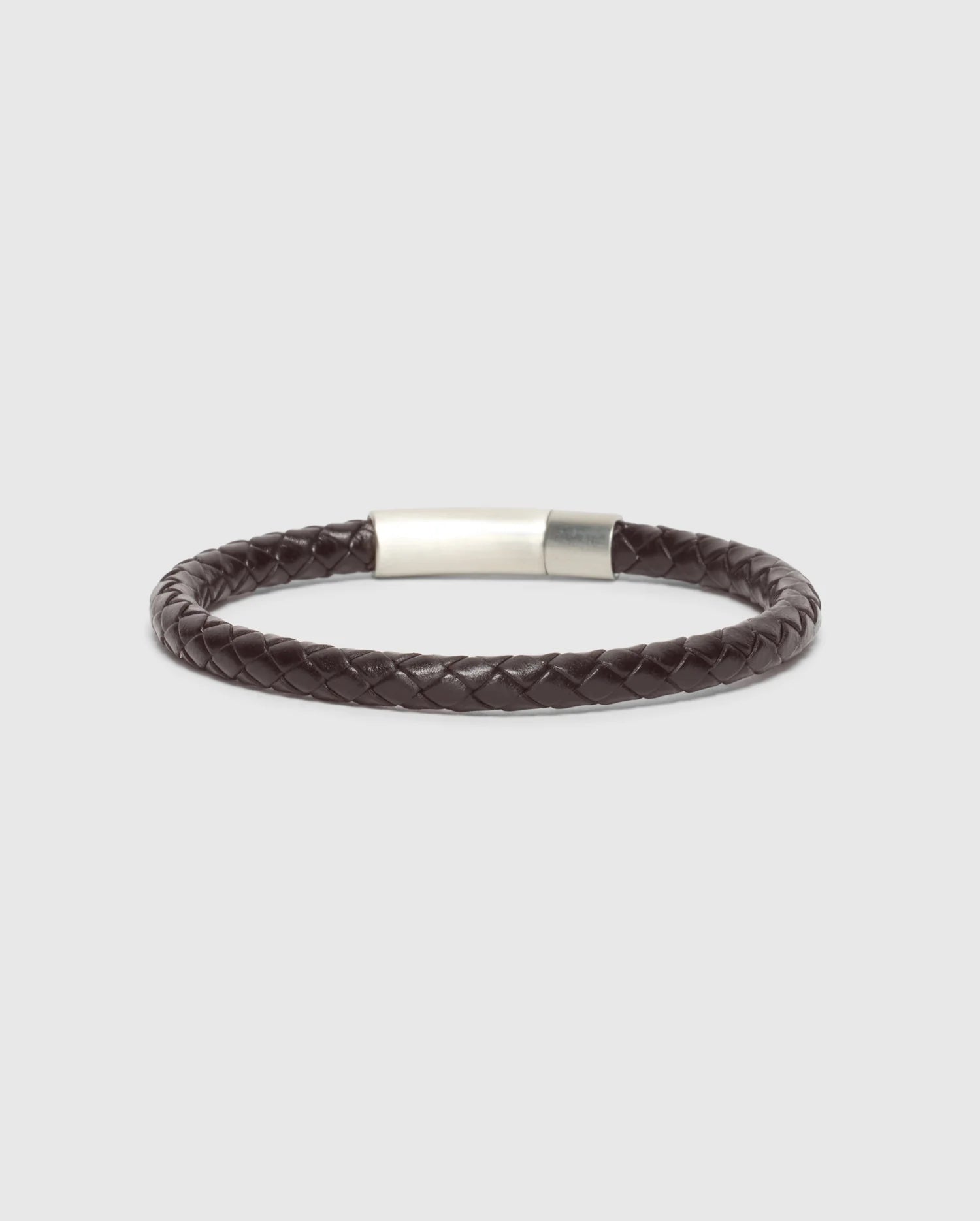 A stylish and elegant accessory, the MEN'S BRAIDED LEATHER BRACELET - B6A371E200 from Psycho Bunny showcases a sophisticated dark brown braided leather design with a sleek polished silver clasp, set against a minimalist light gray backdrop.