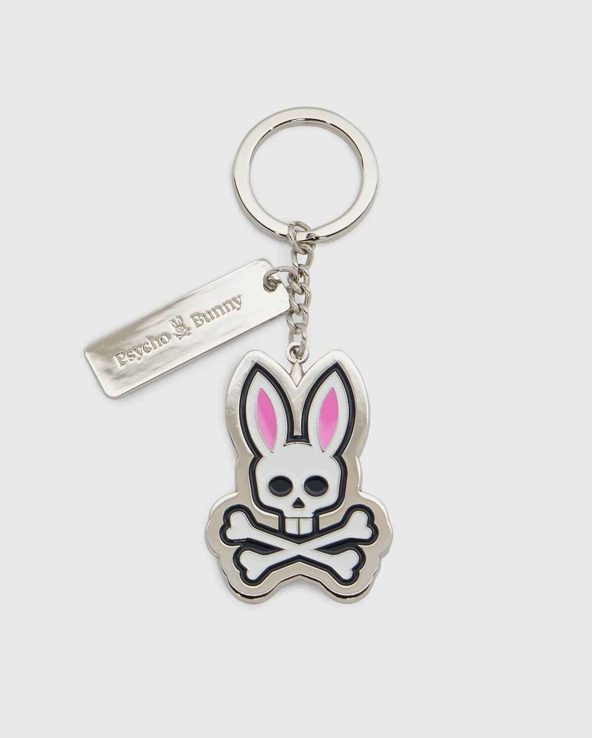 Introducing the CLASSIC BUNNY KEYCHAIN - B6A372E200 from Psycho Bunny, a fashionable metal accessory showcasing a cartoon bunny skull and crossbones design with distinctive pink ears. This practical everyday keychain features a sleek rectangular tag engraved with "Psycho Bunny." Complemented by a silver-colored chain and keyring, it adds a chic touch to your essentials.