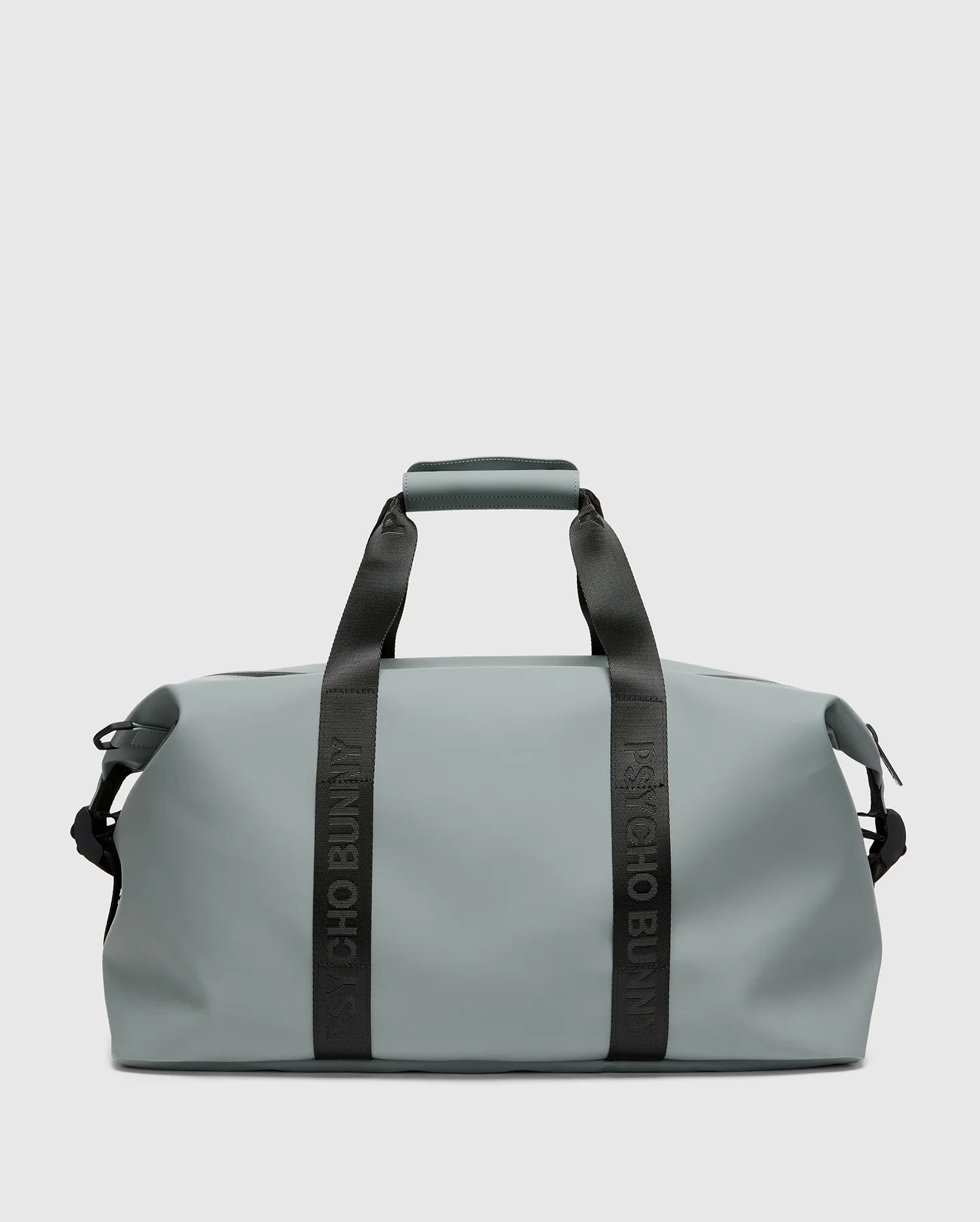 The "MENS DUFFLE BAG - B6A472F200" by Psycho Bunny is a sleek grey carry-all duffel featuring sturdy black handles and strap, the iconic logo, a minimalist design, and smooth texture. It's ideal for packing essentials for travel or gym use.