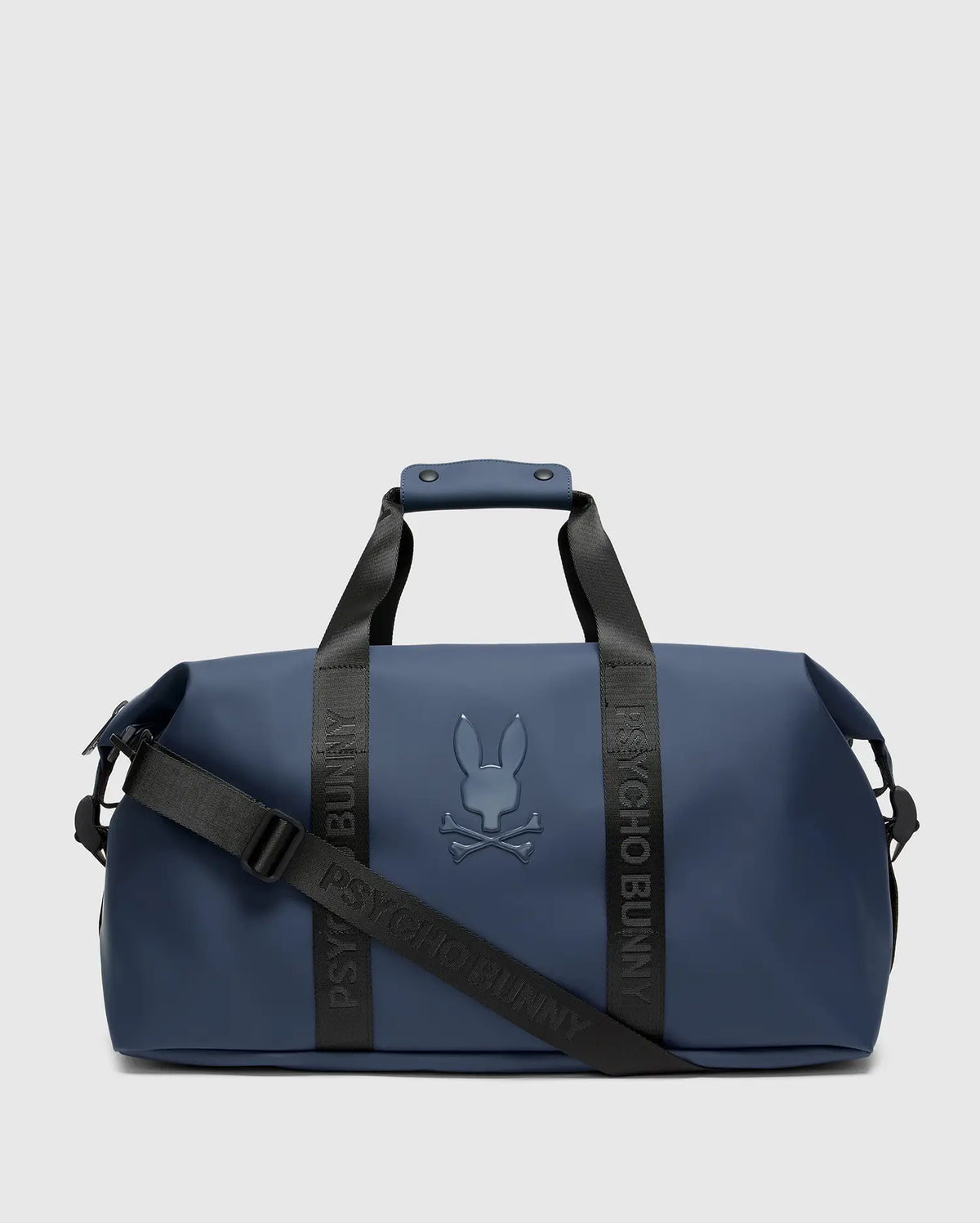 The MENS DUFFLE BAG - B6A472F200 by Psycho Bunny is a sleek blue travel accessory with black straps and handles, featuring their raised bunny with crossbones logo. It includes "Psycho Bunny" on the quality straps and offers a detachable shoulder strap for added convenience.