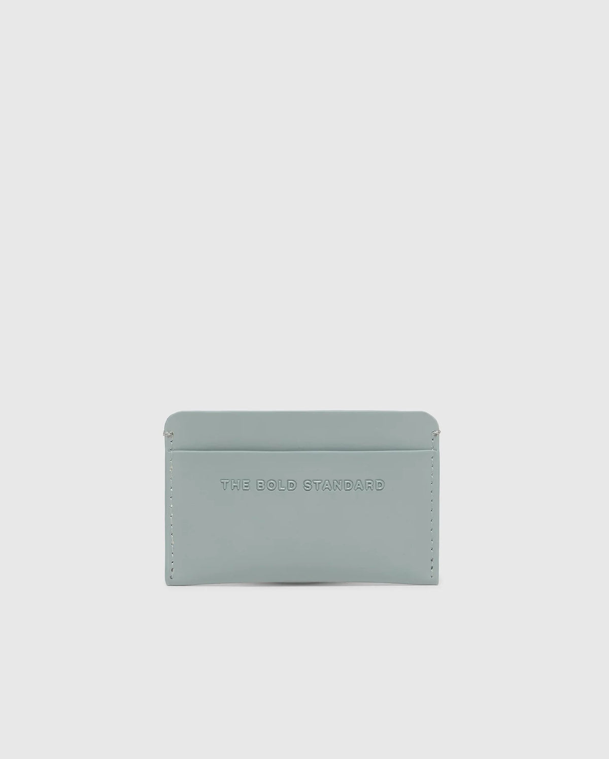 The Psycho Bunny MENS RUBBERIZED CARD CASE - B6A473F200 features "THE BOLD STANDARD" embossed on its light gray, minimalist leather design. Offering security and elegance against a white background, this piece is both stylish and functional.