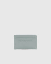The Psycho Bunny MENS RUBBERIZED CARD CASE - B6A473F200 features "THE BOLD STANDARD" embossed on its light gray, minimalist leather design. Offering security and elegance against a white background, this piece is both stylish and functional.