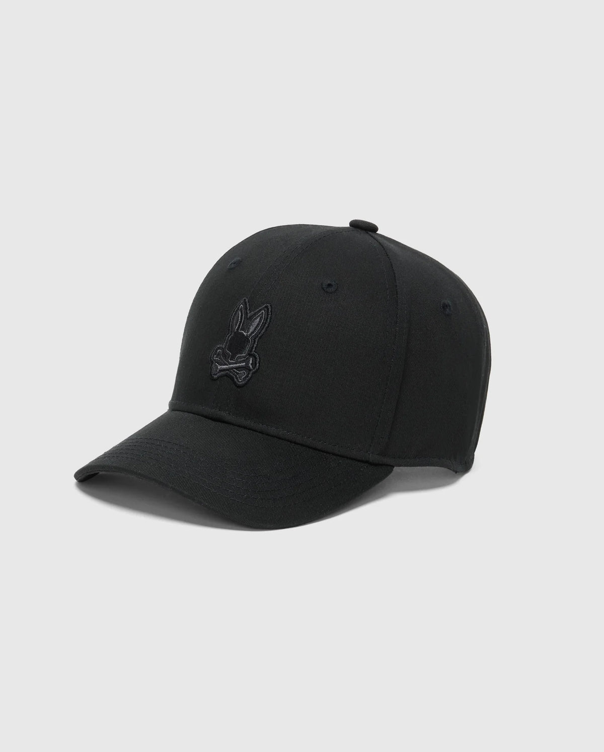 The Psycho Bunny MENS NEW CASTLE GRAPHIC BASEBALL CAP - B6A547F200 is a black cotton twill cap with an animal-like logo, curved brim, and visible stitching. It features an adjustable back strap on a plain light gray background.