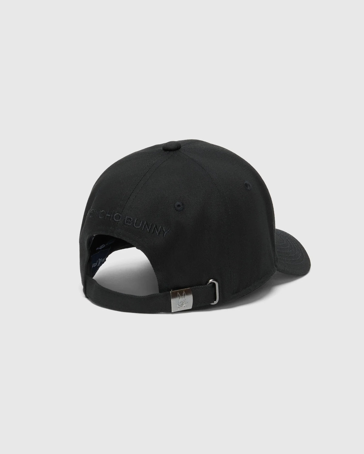 The MENS NEW CASTLE GRAPHIC BASEBALL CAP by Psycho Bunny, made from durable cotton twill, features a metal buckle on the adjustable strap with subtle brand embroidery above the opening. It includes a curved brim and top button for classic style, viewed from the back.