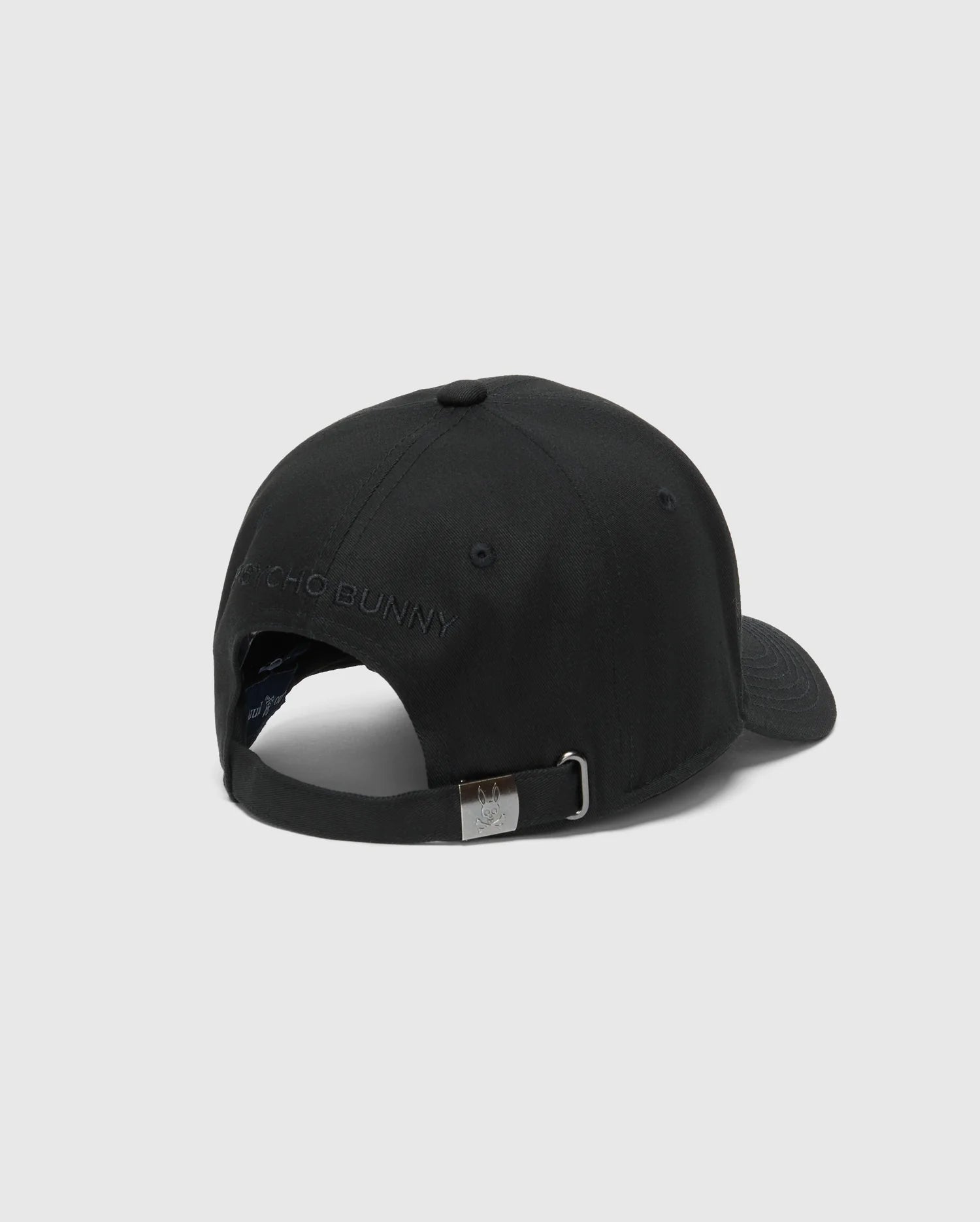 The MENS NEW CASTLE GRAPHIC BASEBALL CAP by Psycho Bunny, made from durable cotton twill, features a metal buckle on the adjustable strap with subtle brand embroidery above the opening. It includes a curved brim and top button for classic style, viewed from the back.