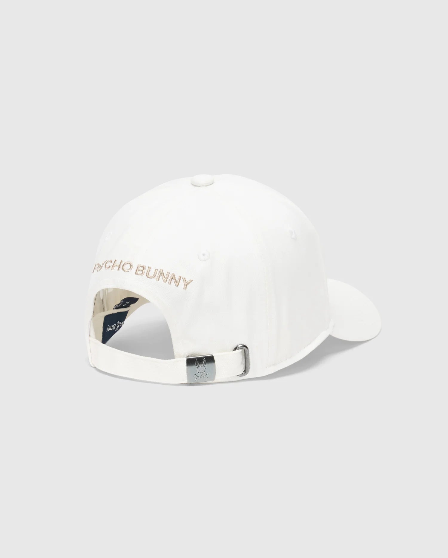 The Men's New Castle Graphic Baseball Cap by Psycho Bunny features white cotton twill, an adjustable strap with a metal buckle at the back, "PSYCHO BUNNY" embroidered in pink on the back panel for a luxurious touch, and a small logo tag near the buckle.