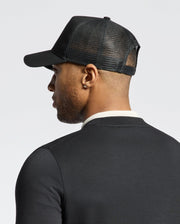 A man in a dark shirt faces away, wearing a Psycho Bunny MENS MELBOURNE GRAPHIC TRUCKER HAT with a snap-back strap.