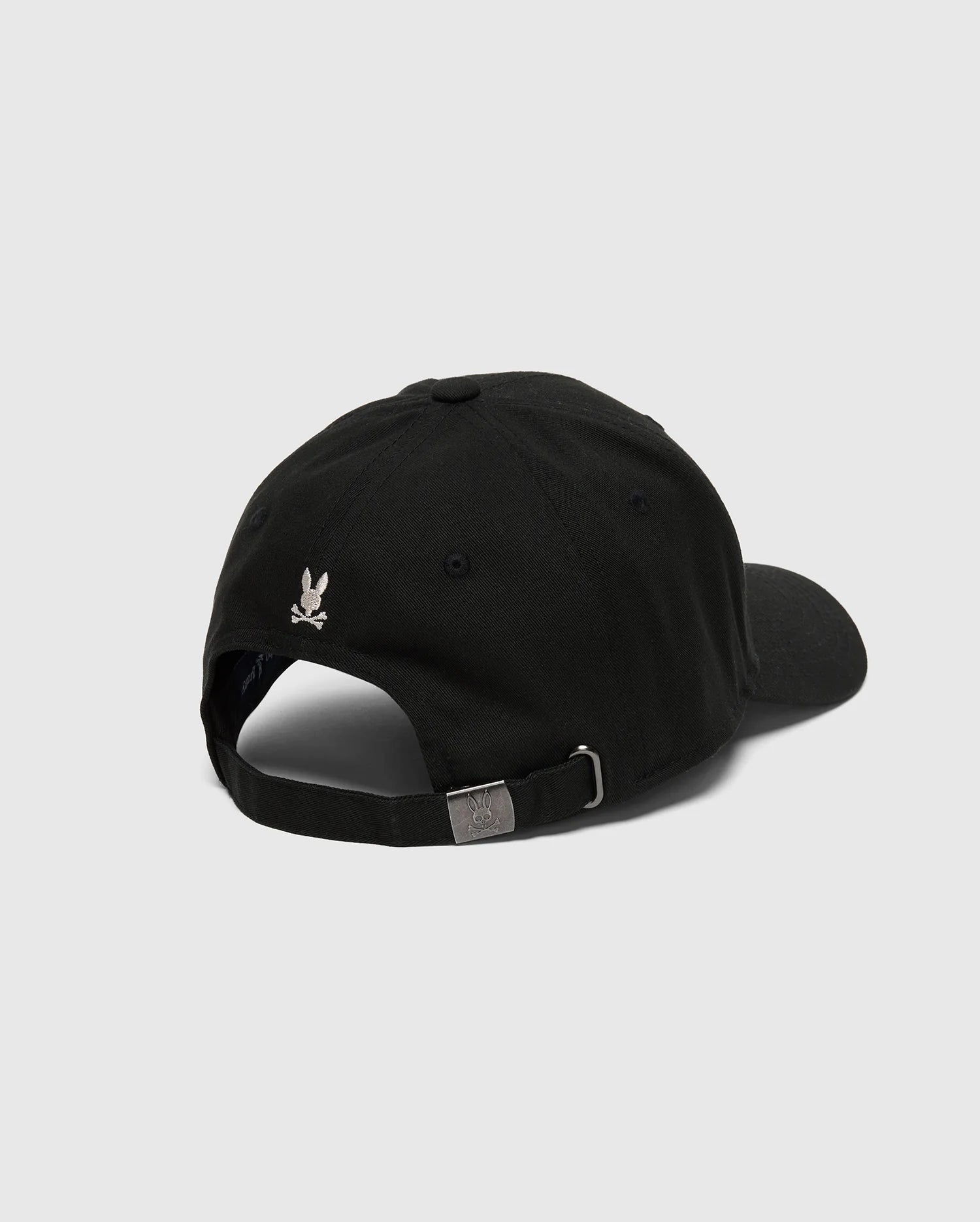 The Psycho Bunny MENS DESERT BASEBALL CAP (B6A549F200) features a black 100% cotton design with a small white eagle logo on the back. Its adjustable strap and metallic buckle are showcased against a light gray background.