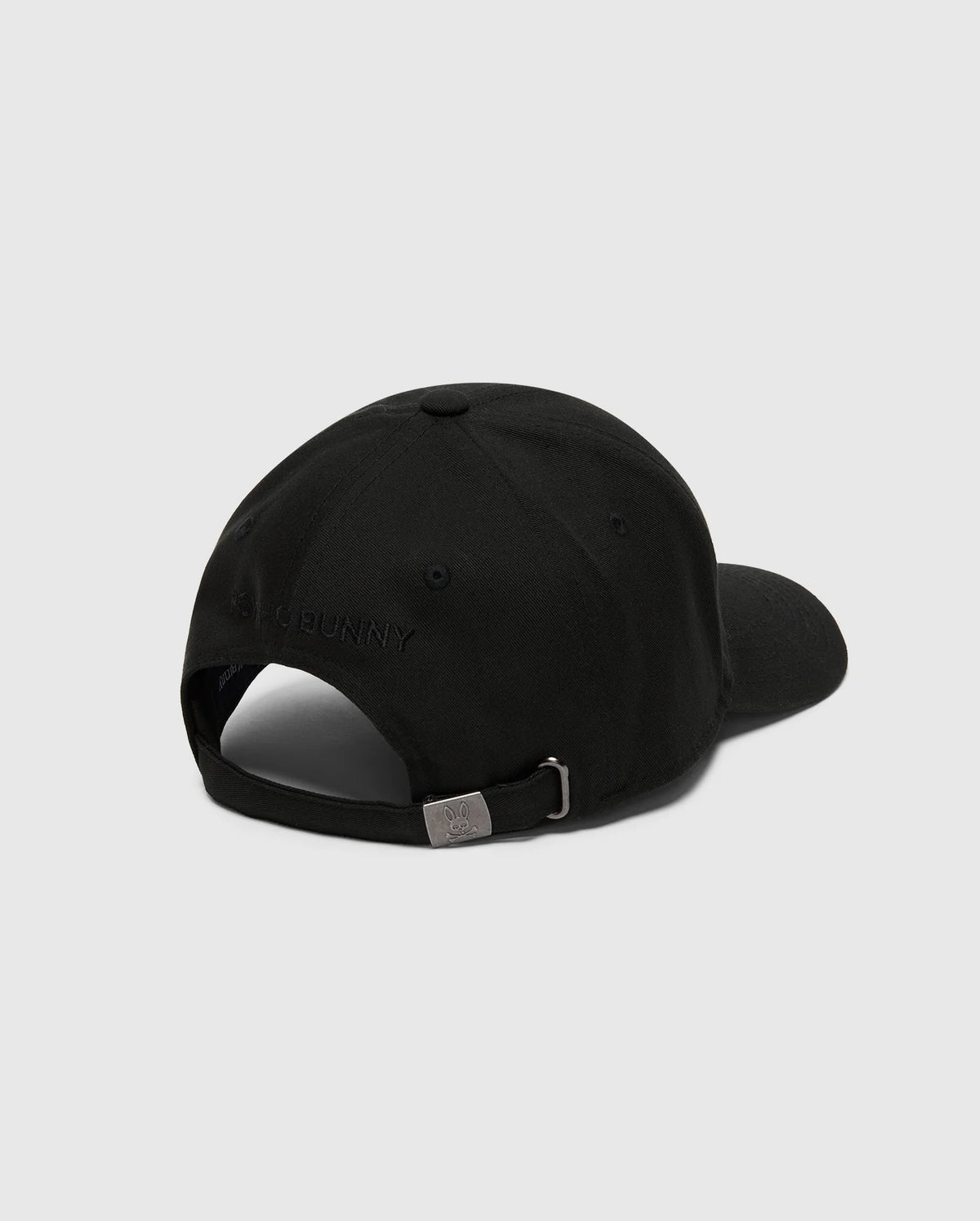The MENS NICHOLSON PB BUNNY GRAPHIC BASEBALL CAP by Psycho Bunny, in black cotton twill with a curved brim, features an adjustable backstrap with a metal clasp and subtle stitching. The PB embroidery is present but not clearly readable against the light gray background.