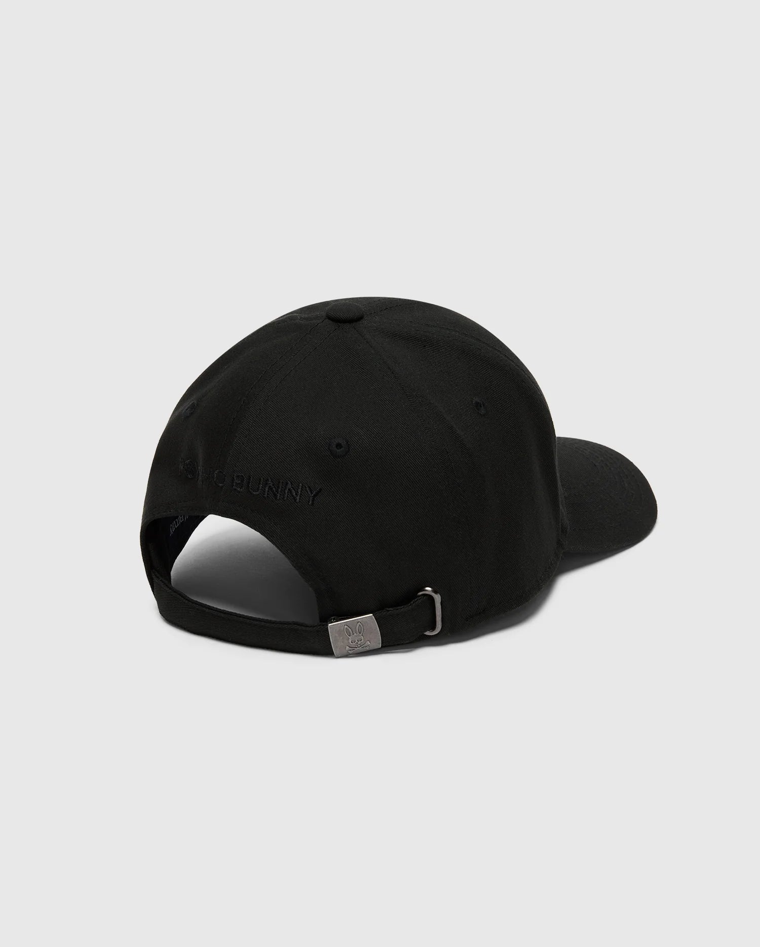 The MENS NICHOLSON PB BUNNY GRAPHIC BASEBALL CAP by Psycho Bunny, in black cotton twill with a curved brim, features an adjustable backstrap with a metal clasp and subtle stitching. The PB embroidery is present but not clearly readable against the light gray background.