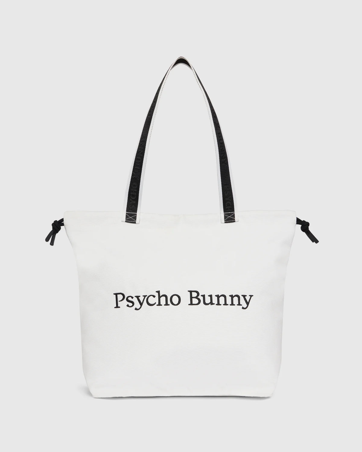 The Psycho Bunny TENNIS TOTE - B6A596C200 is a white canvas tote bag with black handles, featuring the text "Psycho Bunny" on the front. It effortlessly combines style and functionality, making it perfect for tennis enthusiasts.
