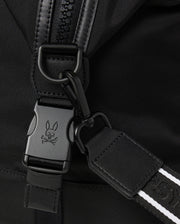 Close-up image of a backpack strap featuring a black buckle with a bunny and crossbones logo engraved on it. The strap includes a black carabiner clip and a white-striped detail to enhance its design, making it perfect for pairing with your Psycho Bunny MENS WEEKENDER BAG - B6A629Z1BG or travel luggage. The fabric is black and textured.