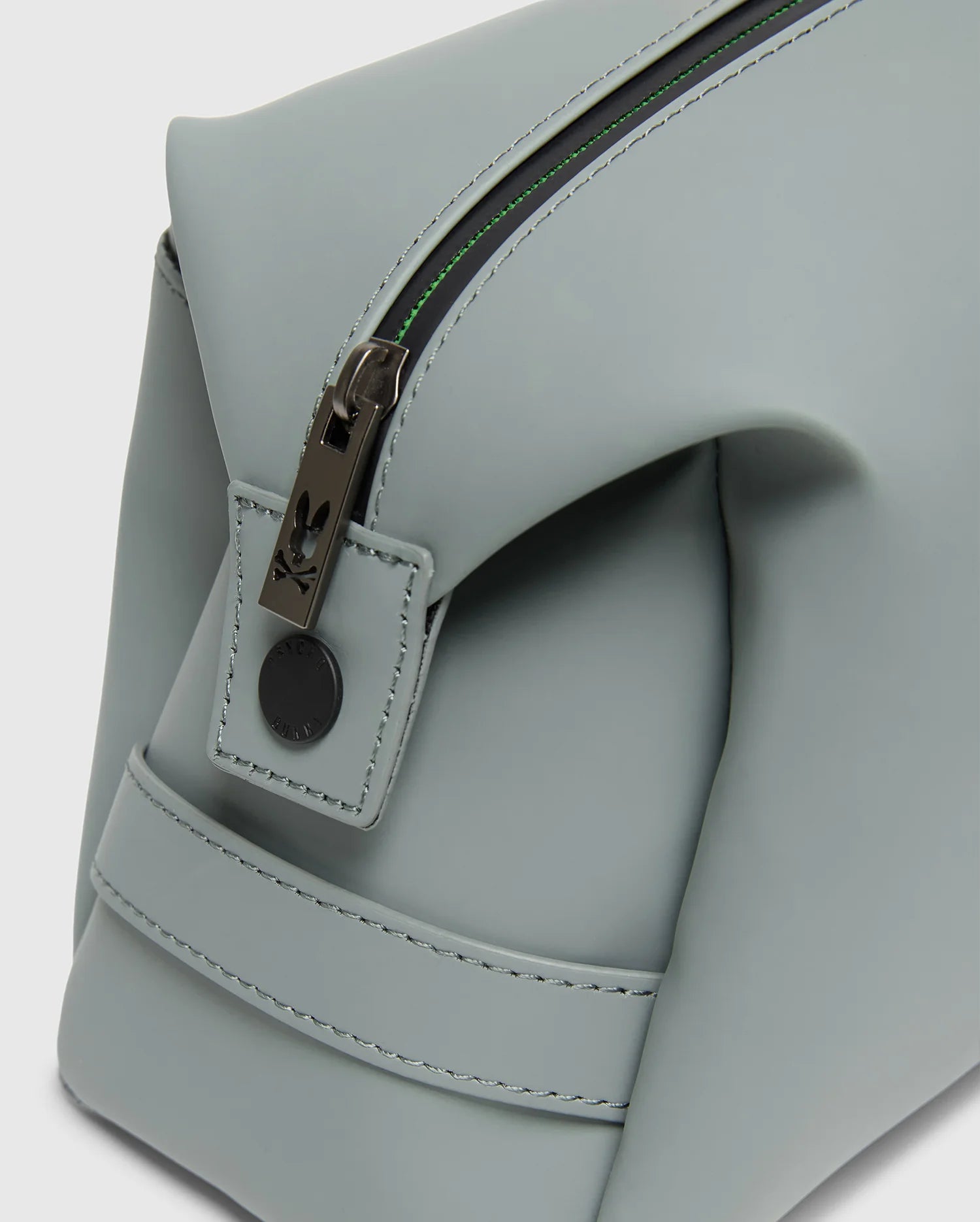 Close-up of the Psycho Bunny MENS TOILETRY KIT - B6A636F200, a light gray, rectangular polyester bag with clean stitching and minimalist design, ideal for organizing essentials. It features a partially open zipper with metal pull and small leather tab.