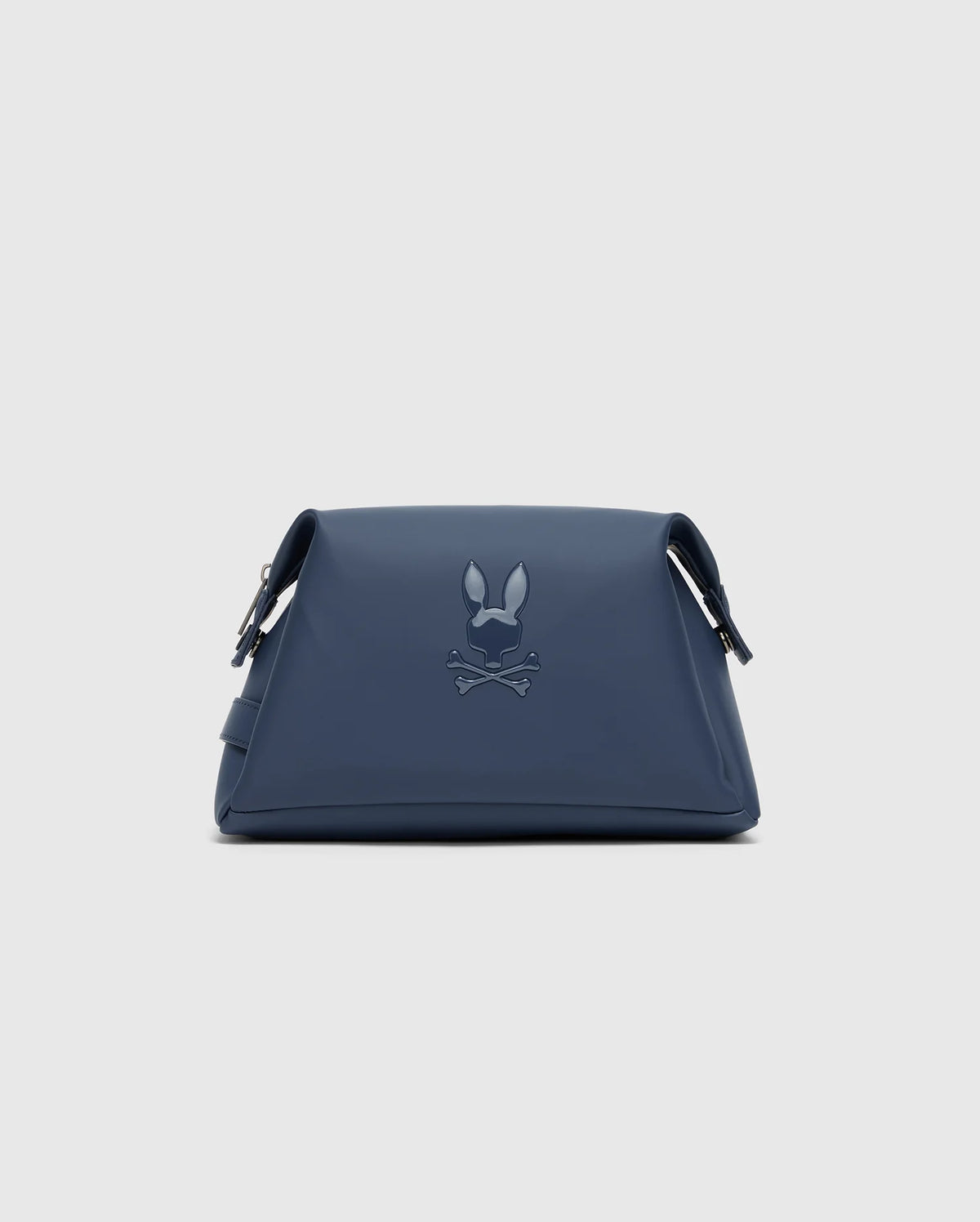 The Psycho Bunny MENS TOILETRY KIT - B6A636F200 is a navy blue triangular bag with an embossed rabbit ears and crossed bones design. Made from 100% polyester, it has adjustable straps and a minimalist style, ideal for organizing essentials on the go.