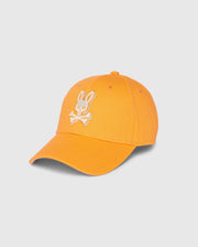 The Psycho Bunny MENS KAYDEN BASEBALL CAP - B6A677C200 is an orange cotton twill baseball cap with a white embroidered bunny logo featuring a head above two crossed bones on the front. It also includes a curved brim and an adjustable strap at the back.