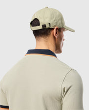 Man photographed from behind wearing a light green polo shirt with dark collar and sleeve trim and a matching light green MENS KAYDEN BASEBALL CAP - B6A677C200 by Psycho Bunny. The light-colored background highlights the neat cotton twill texture of his shirt, subtly adorned with a bunny logo.