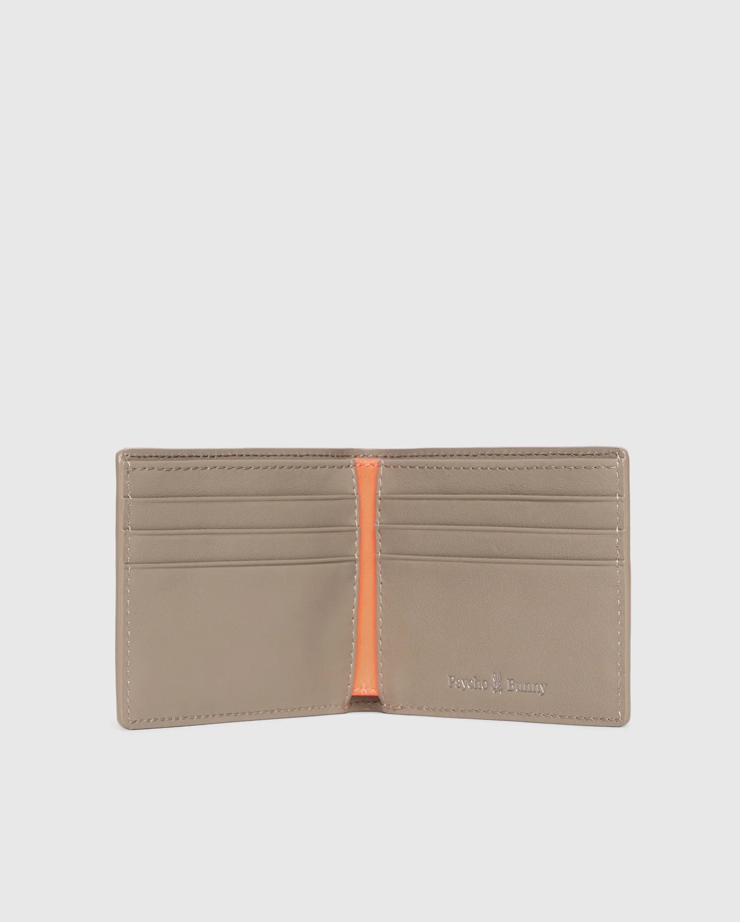 A luxury Psycho Bunny men's leather wallet is open, showcasing multiple card slots and an orange interior accent. The brand name is embossed in silver on the bottom right corner. The plain light gray background highlights the elegance of this premium accessory.