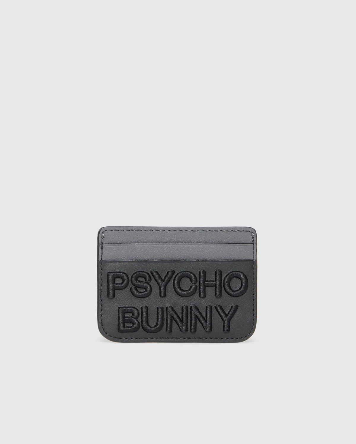 The MENS LEATHER CARD CASE - B6A869D200 by Psycho Bunny is a gray leather card holder with embossed "PSYCHO BUNNY" text on the front and two card slots against a sleek white backdrop. Crafted from premium leather, it offers a minimalist design.
