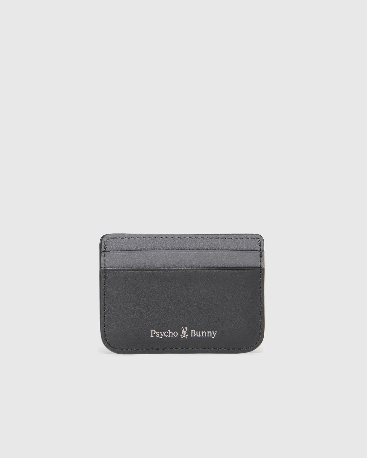 The MENS LEATHER CARD CASE - B6A869D200 from Psycho Bunny is a sleek black rectangular holder made of premium leather, featuring two visible slots. It showcases the iconic "Psycho Bunny" logo and a small white bunny illustration on the bottom, set against a plain white background.