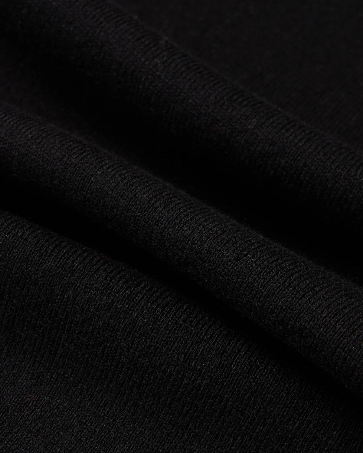 Close-up of the MENS MONROE TWILL PATCH SCARF by Psycho Bunny, highlighting its black wool blend material with intricate texture and weaving pattern featuring multiple folds. The soft, subtly ribbed fabric suggests an air of elegance and luxury textile craftsmanship.