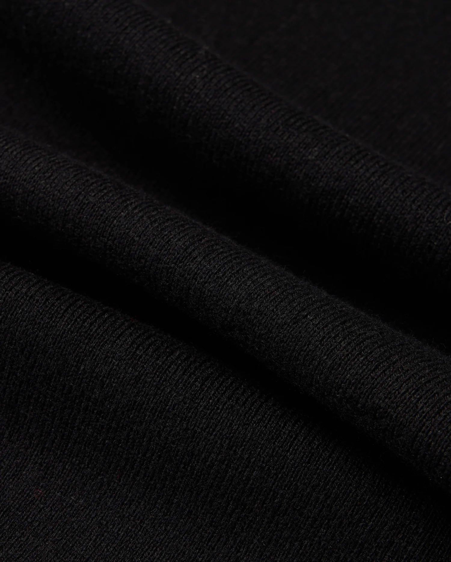 Close-up of the MENS MONROE TWILL PATCH SCARF by Psycho Bunny, highlighting its black wool blend material with intricate texture and weaving pattern featuring multiple folds. The soft, subtly ribbed fabric suggests an air of elegance and luxury textile craftsmanship.